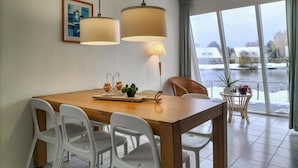A dining area with a wooden table, white chairs, two pendant lights, and a view of a snowy landscape through large windows.