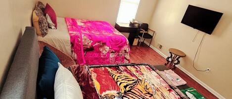 A bedroom with a bed, a desk, a chair, a television, and a window.