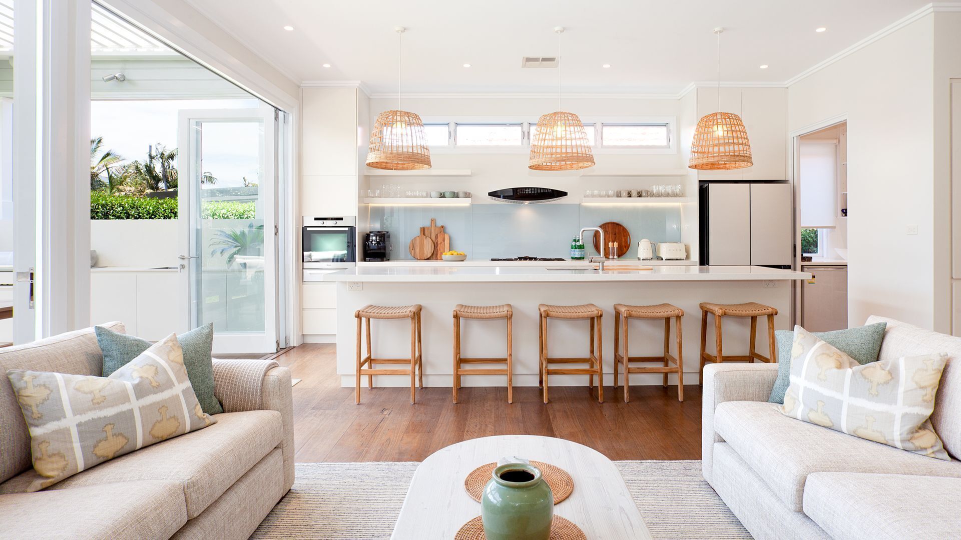 A modern kitchen with a central island, bar stools, and a view to the outdoors.