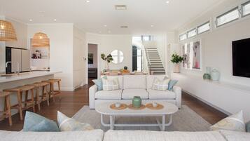 A modern living room with a sofa, coffee table, and bar stools. There is a staircase leading to an upper floor.
