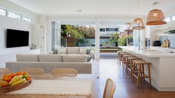 A modern kitchen with a central island, bar stools, and a dining area with a fruit bowl.