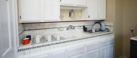 A kitchen with white cabinets, a tiled backsplash, and a countertop with various items.