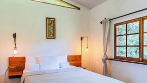Ein Schlafzimmer mit einem Holz-Kopfteil, einem Bett mit weißer Bettwäsche, zwei Wandlampen, einem gerahmten Blumenbild und einem Fenster mit Vorhängen.