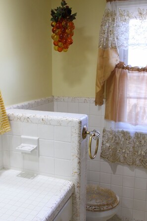 A bathroom with a white tiled shower enclosure, a gold faucet, and a decorative grapevine. - Patsy Cline's Dream Home (Goodlettsville)