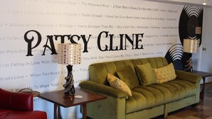 A room with a green sofa, a small table with a lamp, and a wall with a large text sign reading "PATSY GLEN".