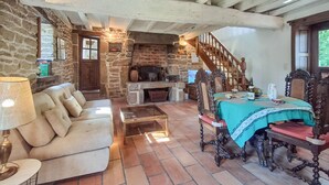 A rustic living room with a stone fireplace, a sofa, a dining table with ornate chairs, and a staircase. - 2 bedroom nice home in Caden (Caden)