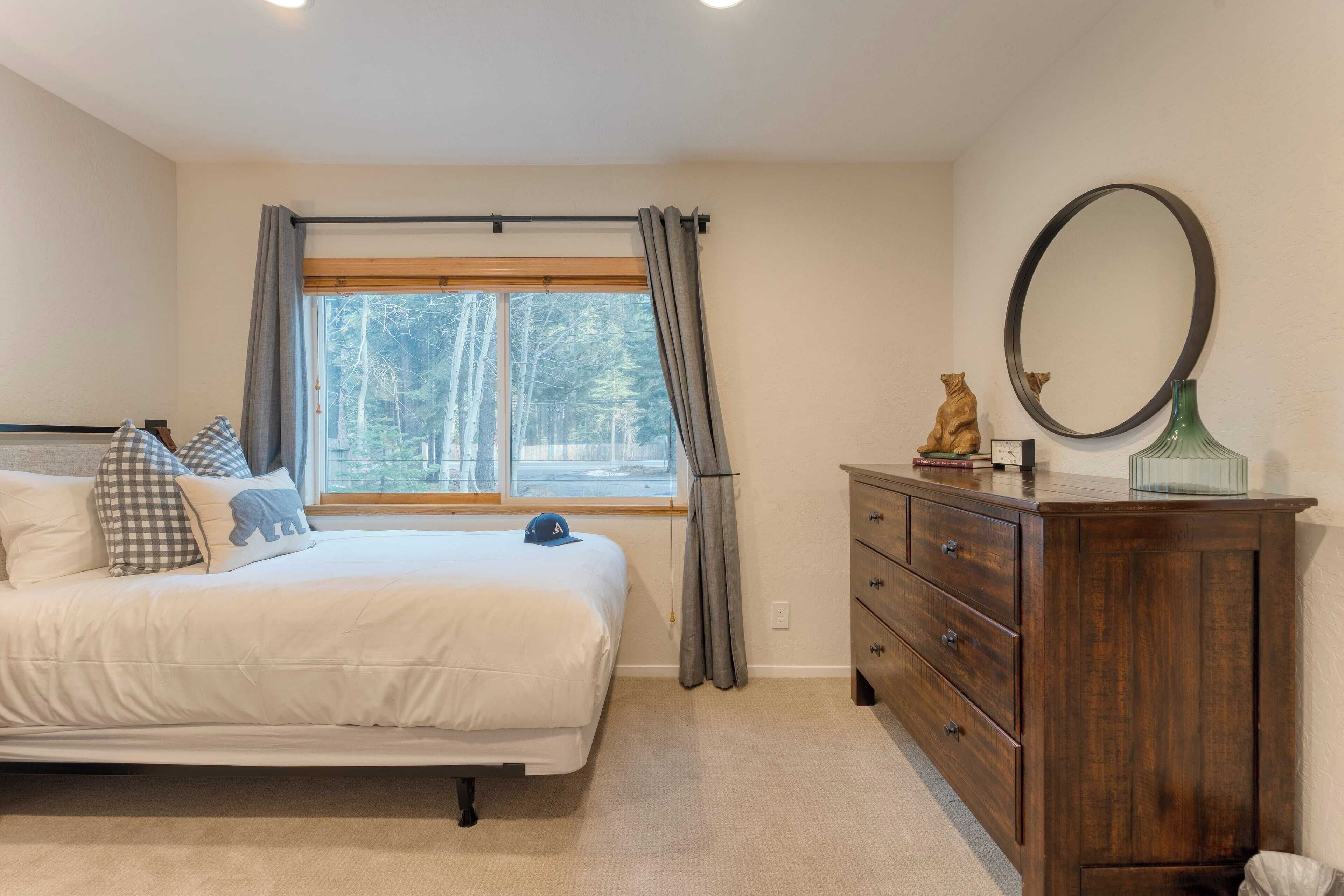 Un dormitorio con cama, cómoda, espejo y ventana con cortinas.
