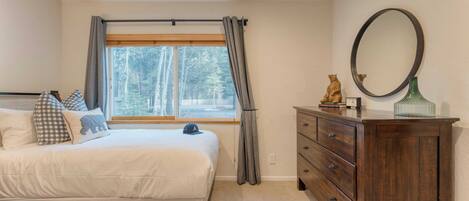 Un dormitorio con cama, cómoda, espejo y ventana con cortinas.