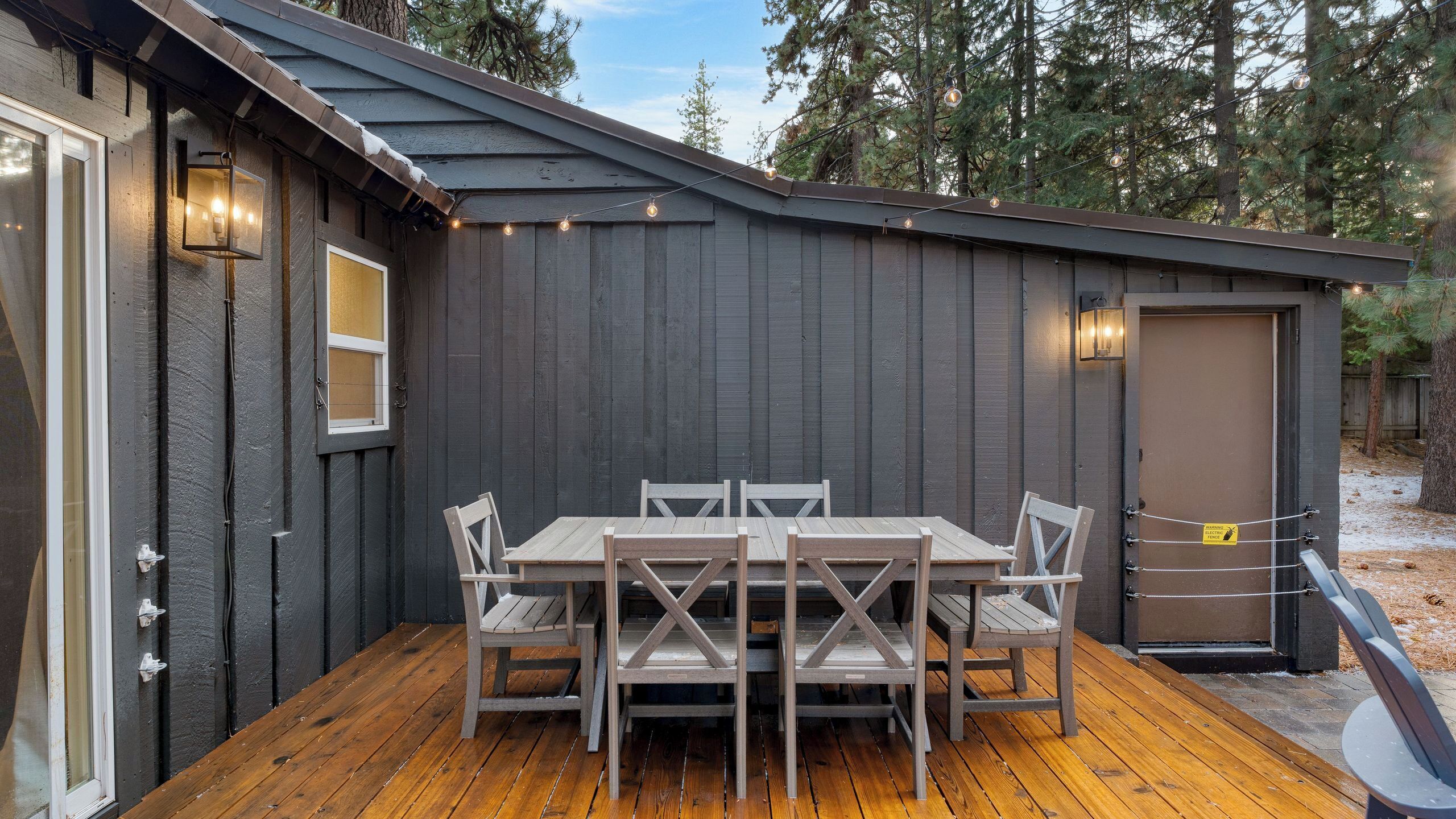 A wooden deck with a table and chairs, a shed with a door, and string lights.