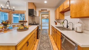 A modern kitchen with wooden cabinets, a central island with fruit, a built-in stove, and a view to the backyard. - Westlake Cabin by Avantstay Hot Tub, Near Skiing, Walk to Restaurants & Lake! (Tahoe City)