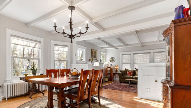 A spacious dining area with a wooden table and chairs, a chandelier, and large windows.