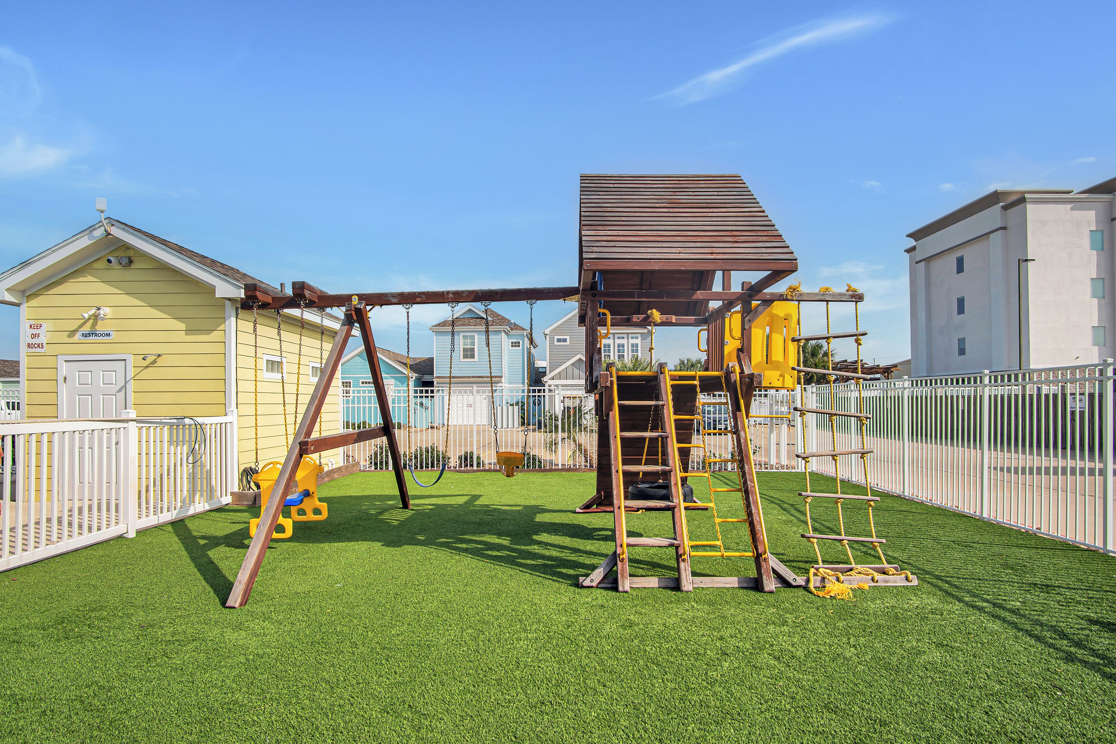 A playground with swings, a climbing structure, and a fenced area.