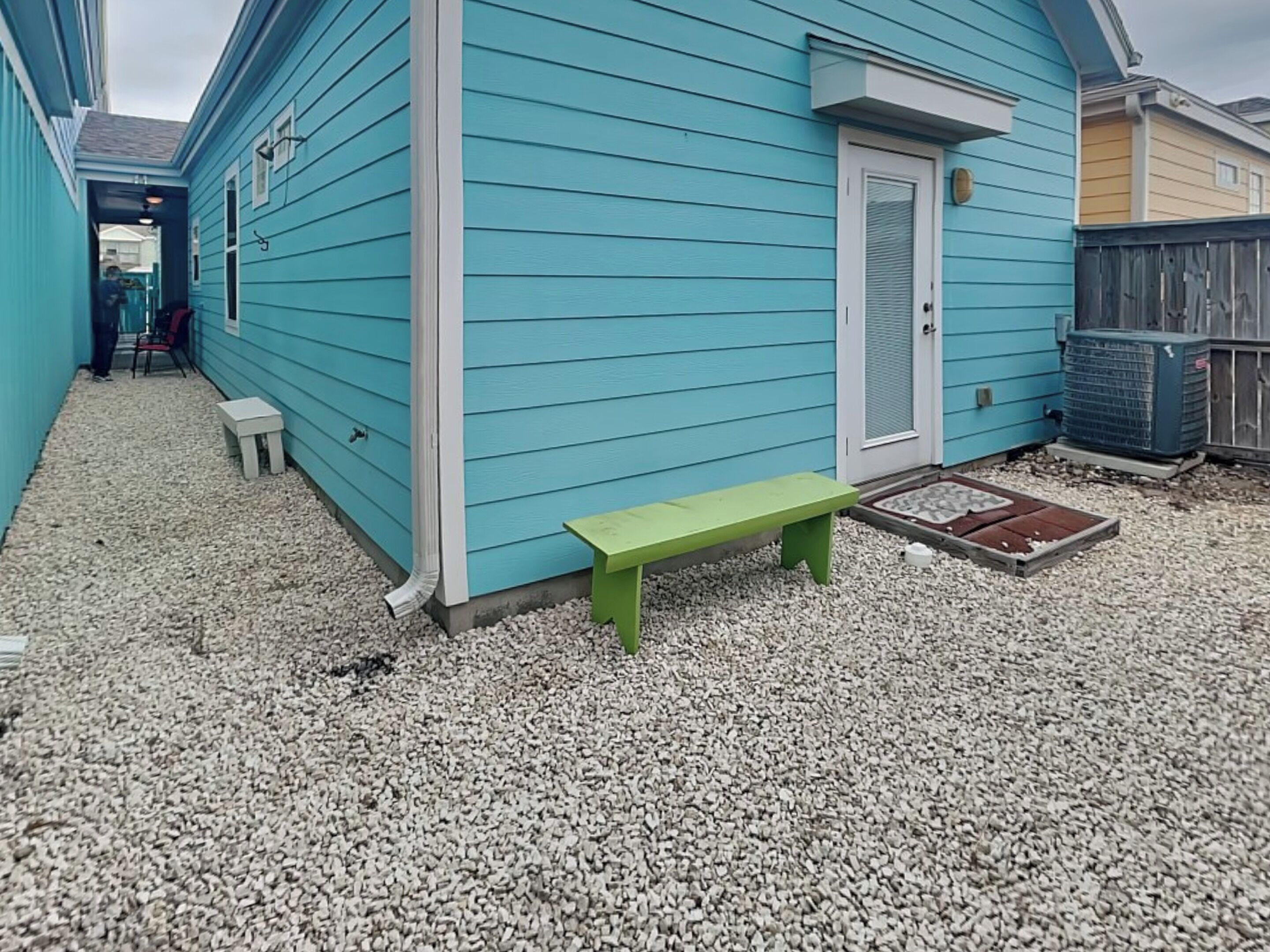 A blue house with a green bench, a white door, and a small white table.