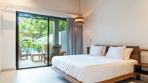 A modern bedroom with a large bed, a wooden headboard, and a sliding glass door leading to an outdoor area with furniture.