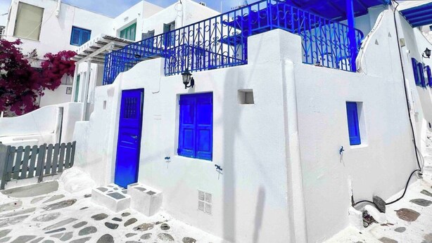 Un edificio blanco con puertas y ventanas azules, una calle empedrada de piedra y una barandilla azul en el balcón.