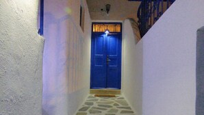 Un estrecho pasillo empedrado de piedra, con una puerta azul al final, que conduce a una habitación con pared blanca y un marco de madera.