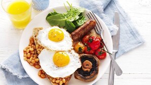 Ein Teller mit Frühstückspeisen, darunter Eier, Bohnen, Tomaten und Grünzeug.