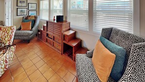 A living room with patterned sofas, a wooden cabinet, and a tiled floor. - The Hidden Porpoise by Silver Sands Vacation Rentals (Port Aransas)