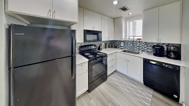 A modern kitchen with stainless steel appliances, white cabinetry, and a patterned backsplash. - Coastal Hideaway by Silver Sands Vacation Rentals (Port Aransas)
