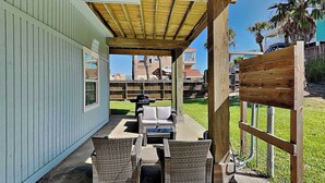 An outdoor patio with wicker furniture, a grill, and a view of a residential area. - Coastal Hideaway by Silver Sands Vacation Rentals (Port Aransas)