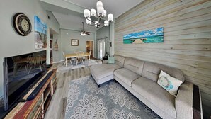A living room with a sofa, a television, a wooden wall, and a patterned rug. - Coastal Hideaway by Silver Sands Vacation Rentals (Port Aransas)