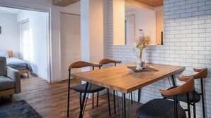 A modern dining area with a wooden table and chairs, a vase with flowers, and a white brick wall. - ZABO HILLS 203 (Sapporo)