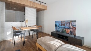 A modern living room with a wooden ceiling, a dining area with a table and chairs, a large TV on a stand, and a bed. - ZABO HILLS 203 (Sapporo)