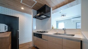 A modern kitchen with a black range hood, white tiled backsplash, wooden cabinets, and a stainless steel sink. - ZABO HILLS 203 (Sapporo)