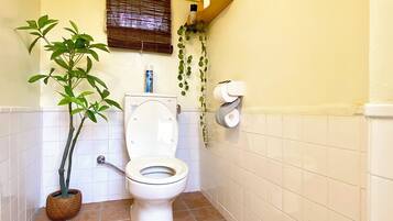 A small bathroom with a toilet, a potted plant, and a window with blinds.