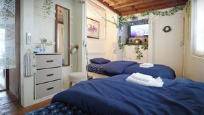A room with two beds, a wooden ceiling, a white wardrobe, a small stool, and a television on the wall.