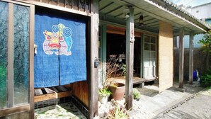 A traditional Japanese house with a wooden exterior, a tiled entrance, and a blue curtain with a lion design.