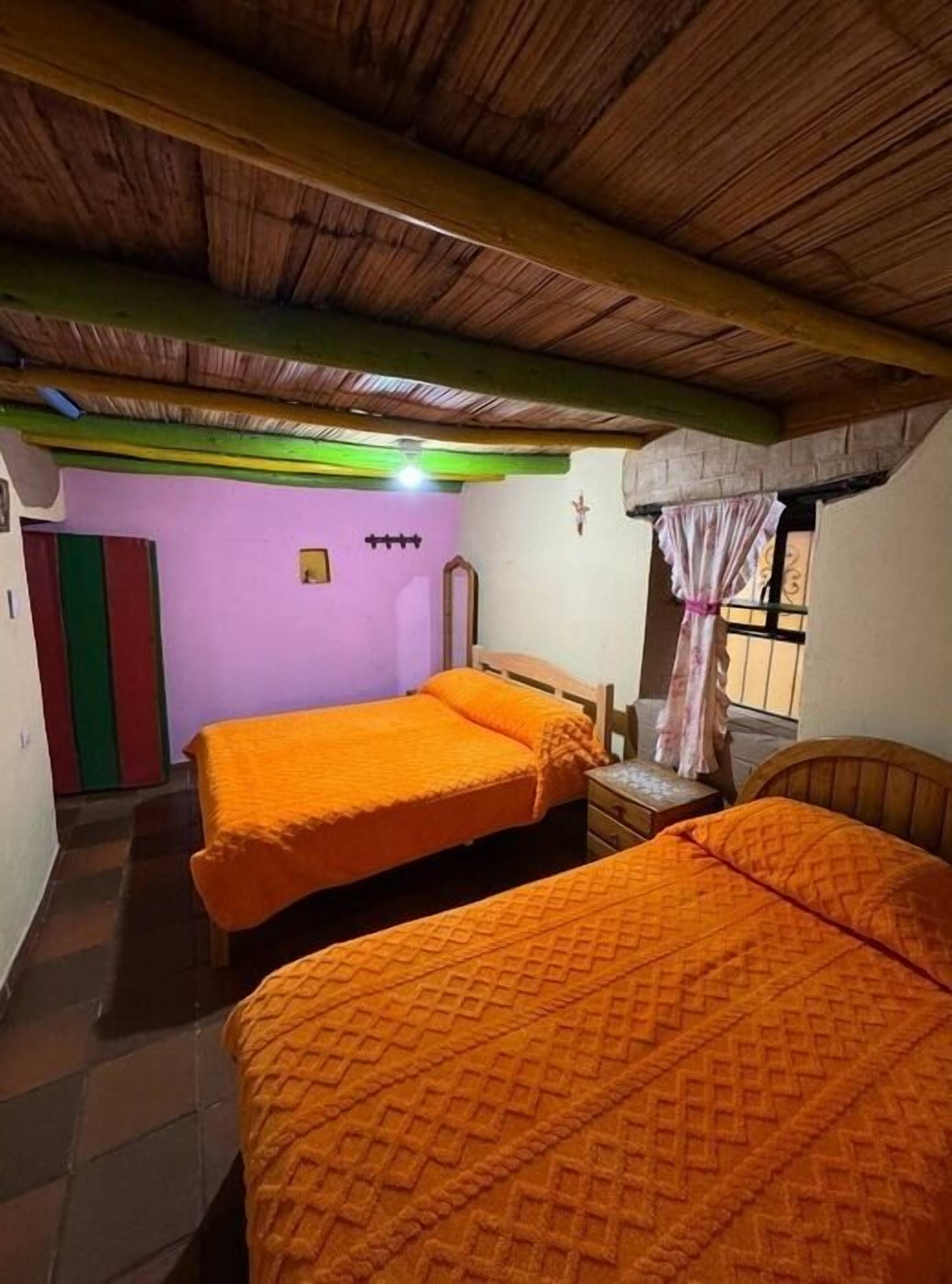 Quarto com duas camas, teto de madeira, parede roxa e janela com cortina.
