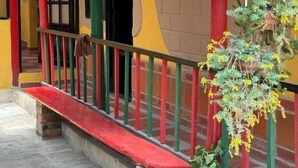Een kleurrijk gebouw met een rode en gele gevel, een groene balustrade en potplanten op de veranda.