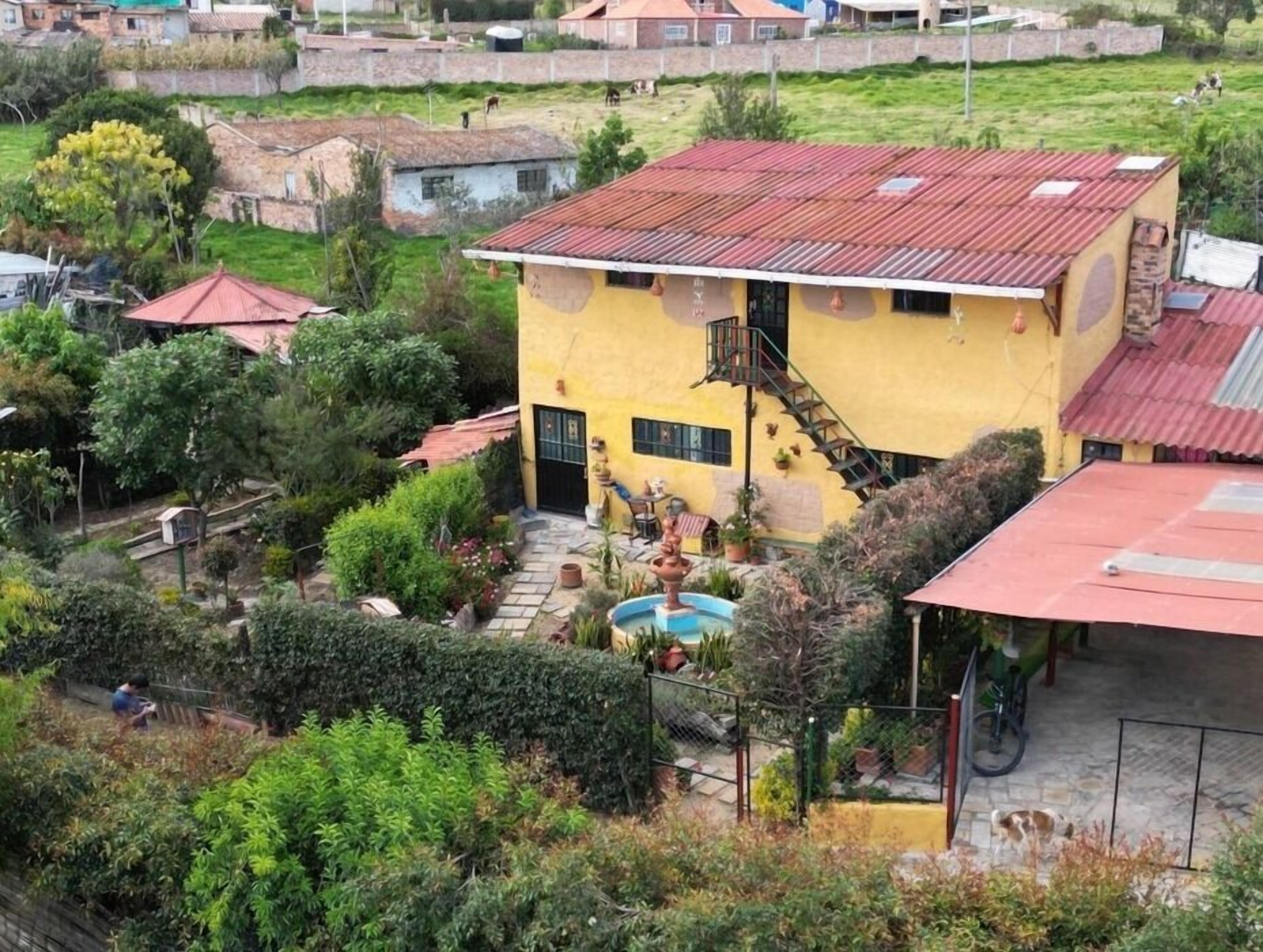 A yellow building with a red roof, surrounded by greenery and a swimming pool.
