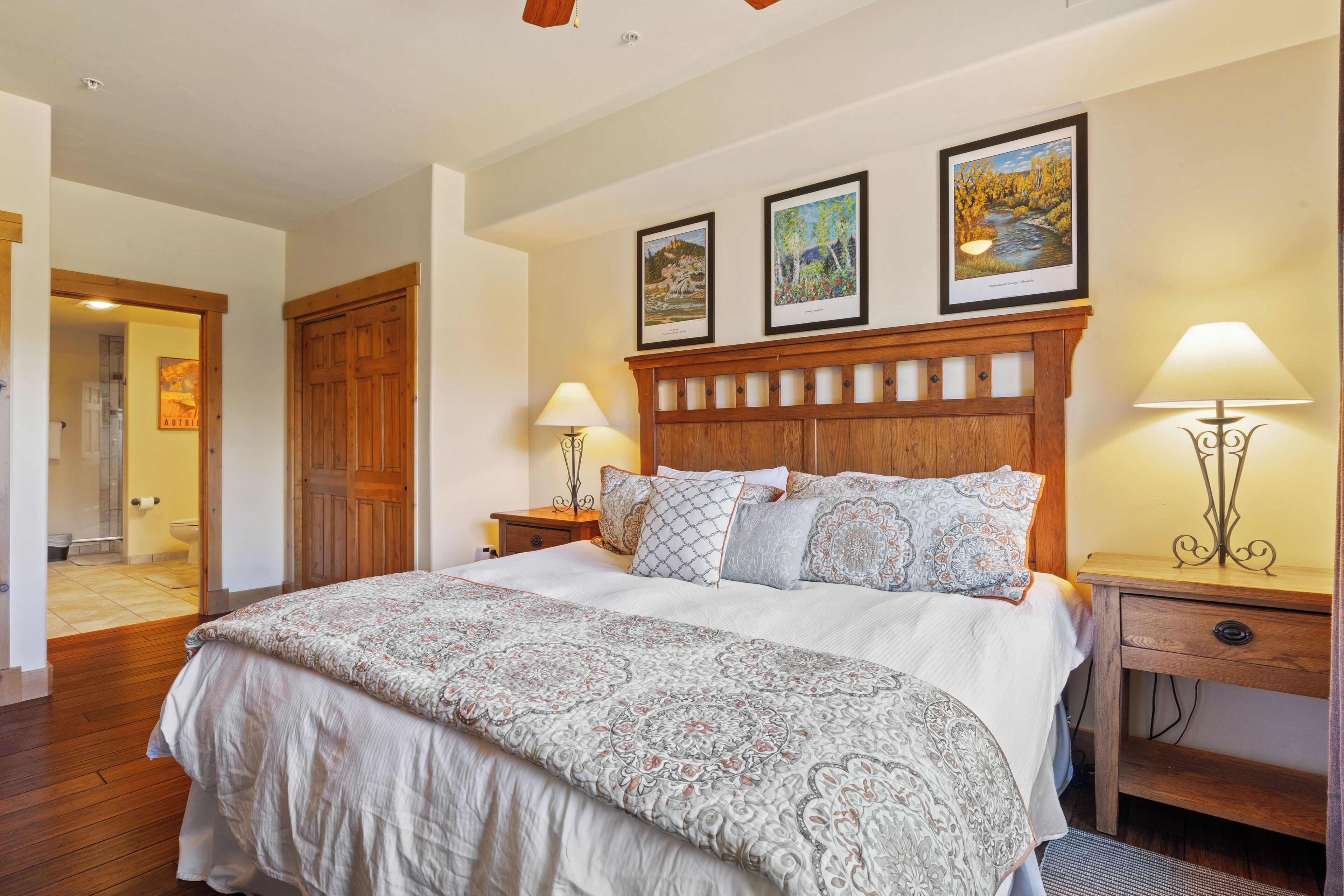 A bedroom with a large bed, wooden headboard, two bedside tables with lamps, and framed artwork on the wall.