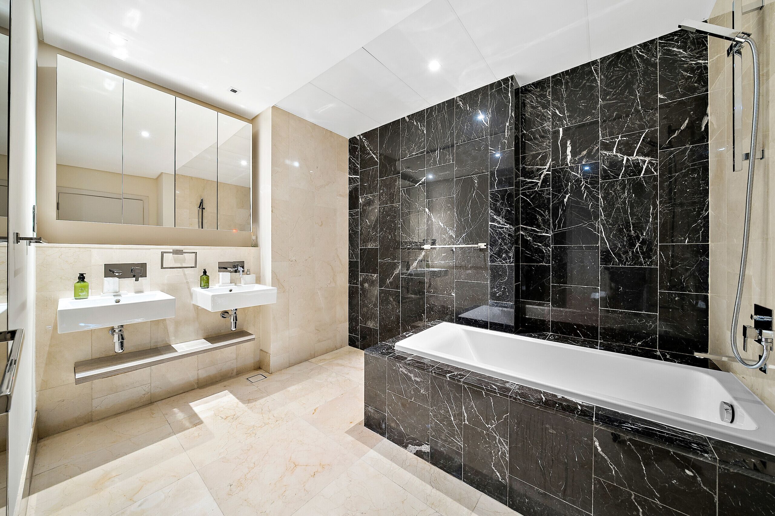 A modern bathroom with two sinks, a large mirror, and a bathtub.