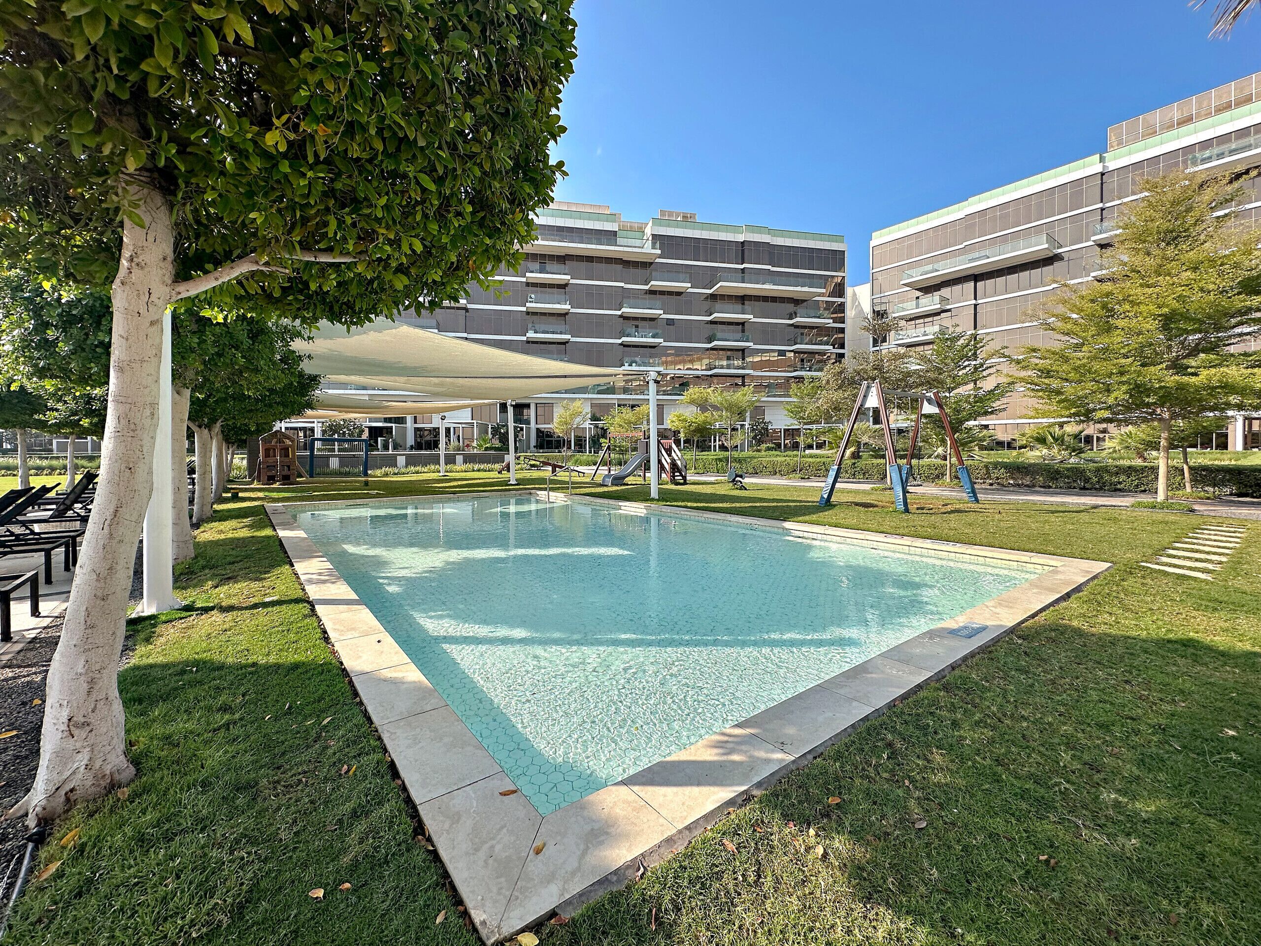 A rectangular swimming pool with a tiled edge, surrounded by grass and trees.