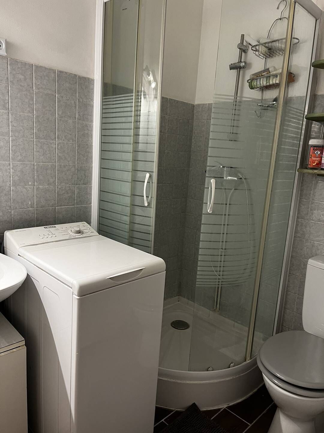 A compact bathroom with a glass-enclosed shower, a washing machine, and a toilet.