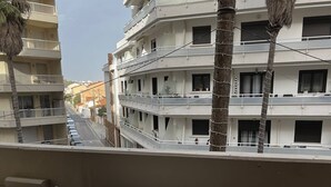 Un balcon avec une table et des chaises, donnant sur une rue bordée d’immeubles et de palmiers.