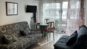Un salon moderne comprenant un canapé, une table à manger avec des chaises, un téléviseur et une grande fenêtre avec des rideaux.