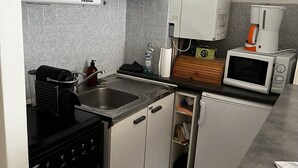Une cuisine de taille réduite avec des meubles blancs, une cuisinière noire, un four à micro-ondes et une machine à café.