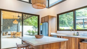 Une cuisine moderne dotée d’un grand îlot central, de tabourets de bar en bois et offrant une vue sur l’extérieur grâce à de grandes fenêtres.
