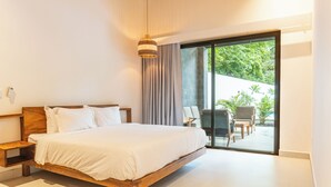 Une chambre moderne avec un grand lit, une tête de lit en bois, une table de chevet et une vue sur un patio aménagé avec du mobilier d’extérieur.