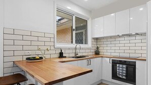 A modern kitchen with white cabinets, a wooden countertop, a built-in oven, and a window above the sink. - 3 bedroom, pet friendly home CBD (Warrnambool)