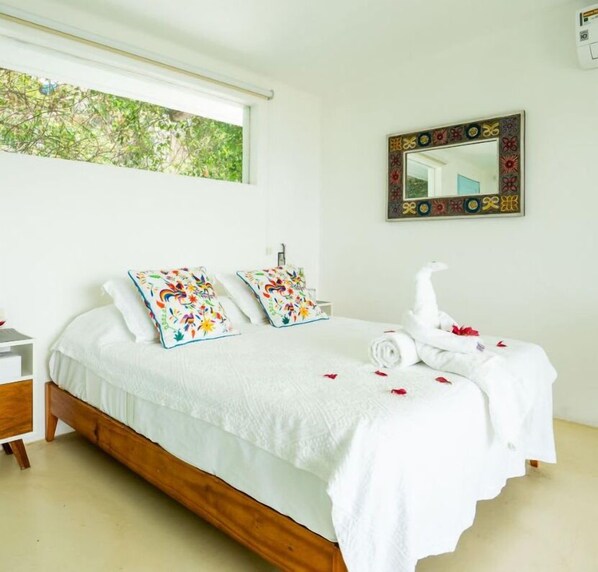A neatly made bed with white bedding and colorful pillows, a bedside table with a lamp, and a window with a view of greenery. - Luxury House Pool fire Pit & Lake view (Jojutla)