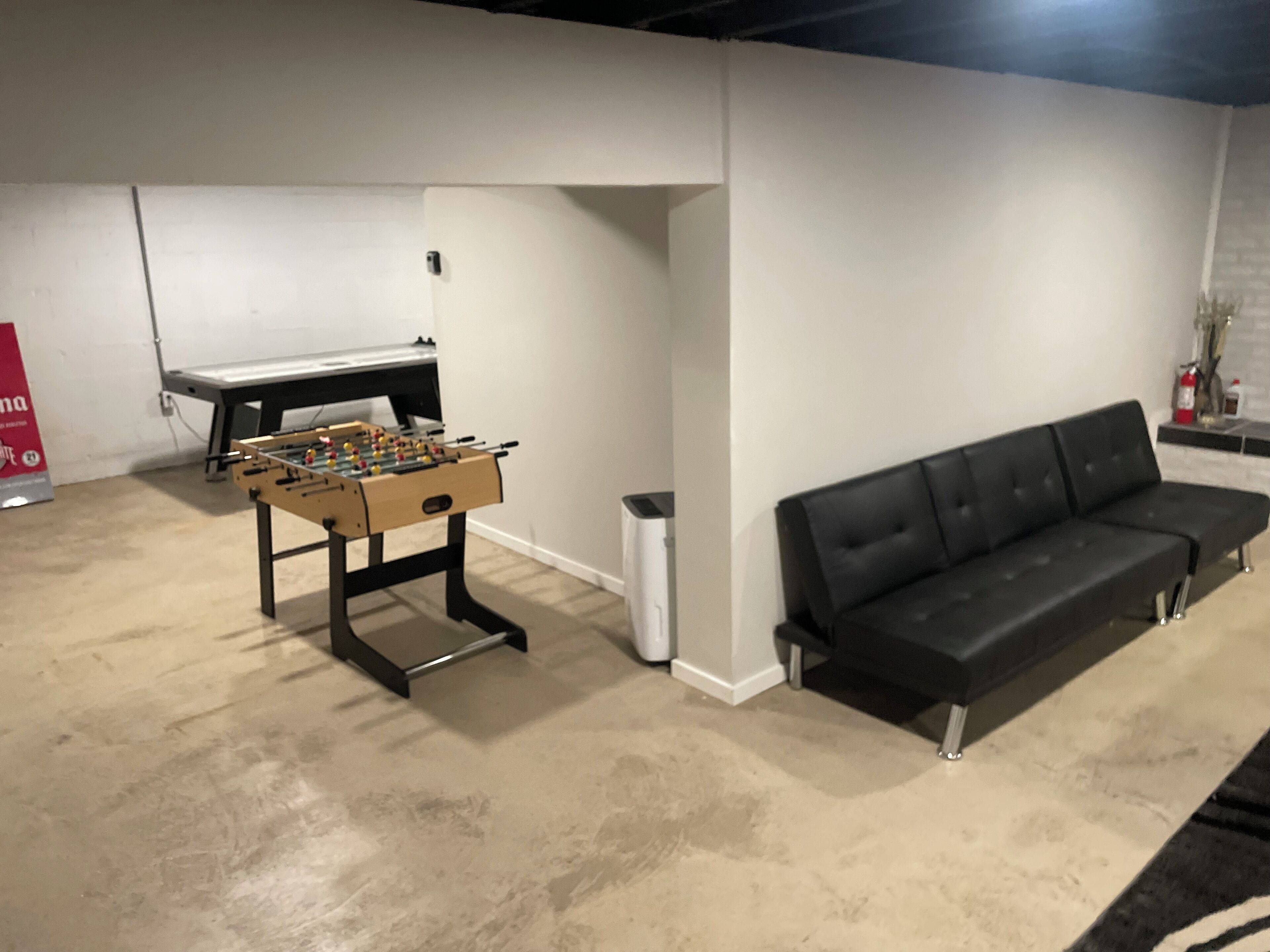 A room with a foosball table, a black sofa, and a white wall.