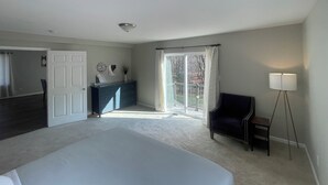 A bedroom with a large bed, a dresser, a chair, a lamp, and a sliding glass door leading to a balcony. - Charming countryside home in the heart of Amish Country (Fredericktown)