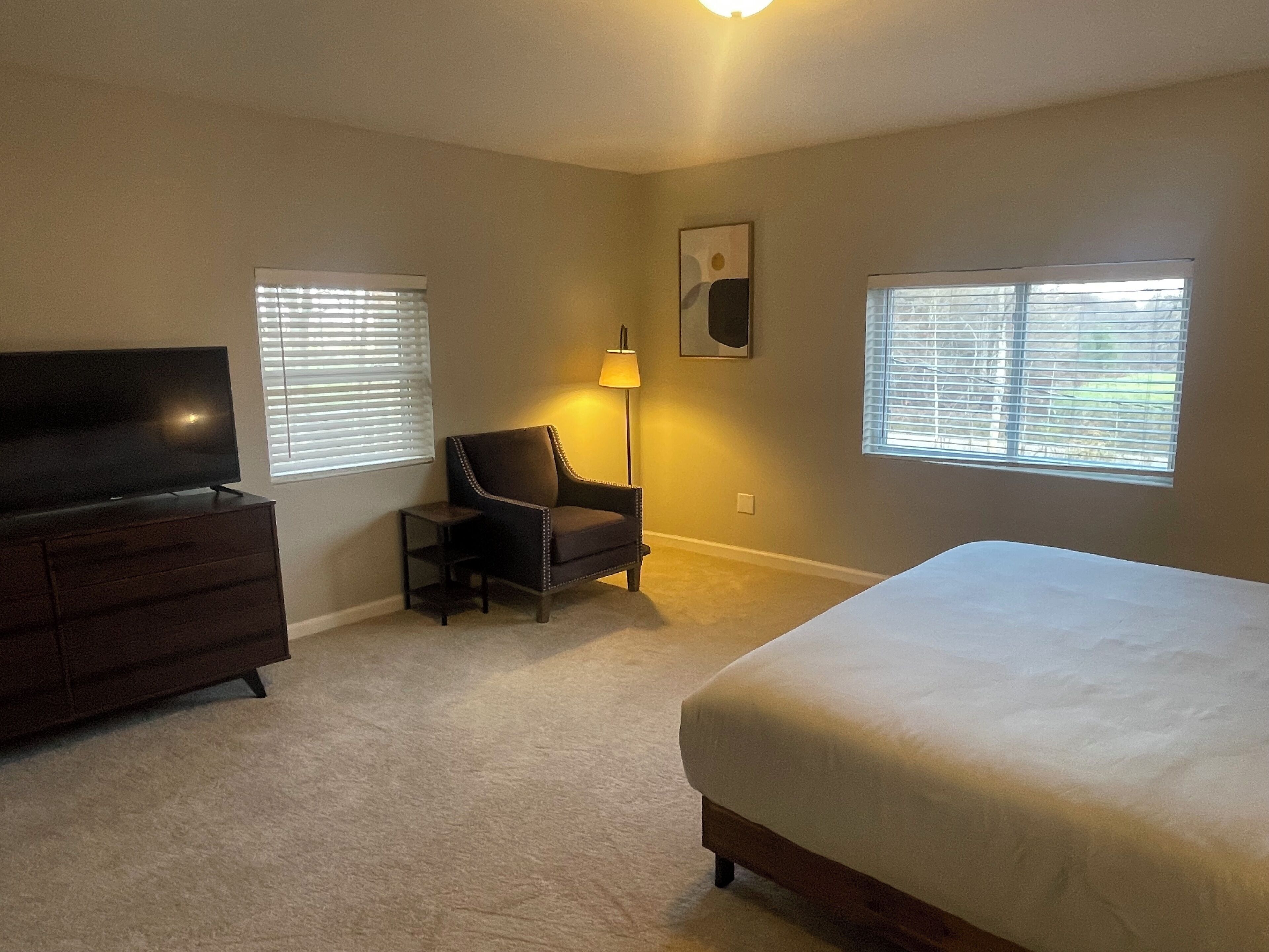 A bedroom with a bed, a TV, a chair, and a lamp.