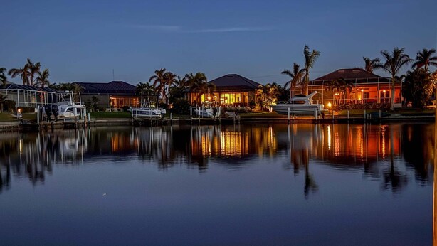 Un puerto deportivo al atardecer con barcos amarrados, un edificio con iluminación cálida y palmeras.