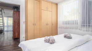 Une chambre à coucher avec un lit double, une armoire en bois et une vue sur l’extérieur à travers des rideaux légers.